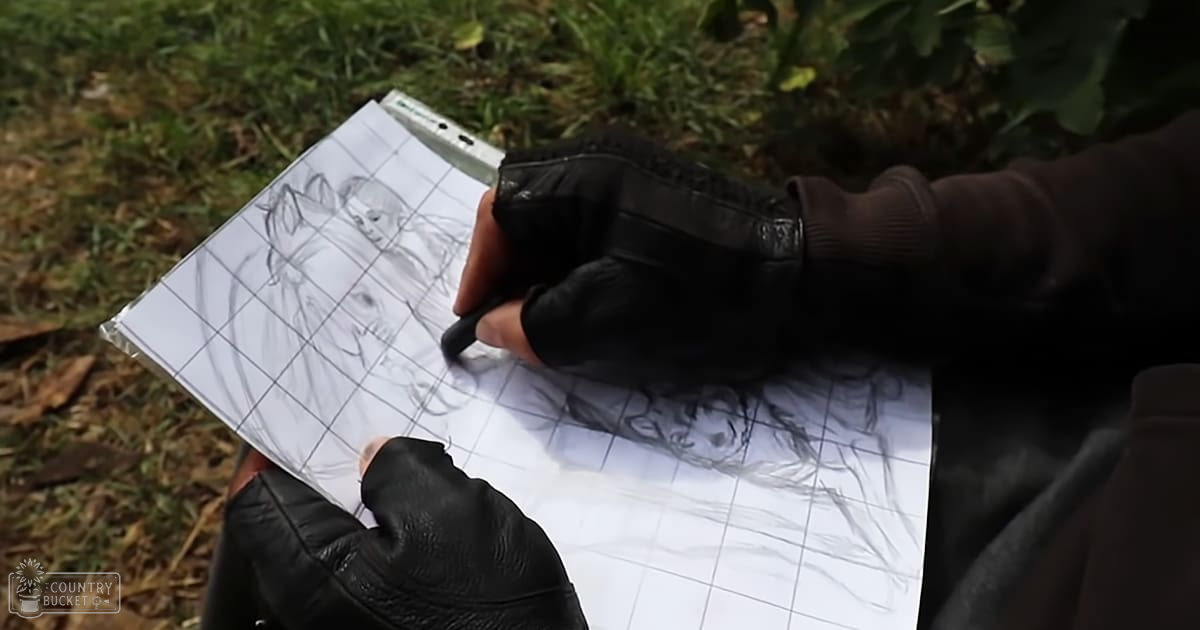 An adult male drawing outdoors on grid paper with a horse's head and neck sketched using pencil.