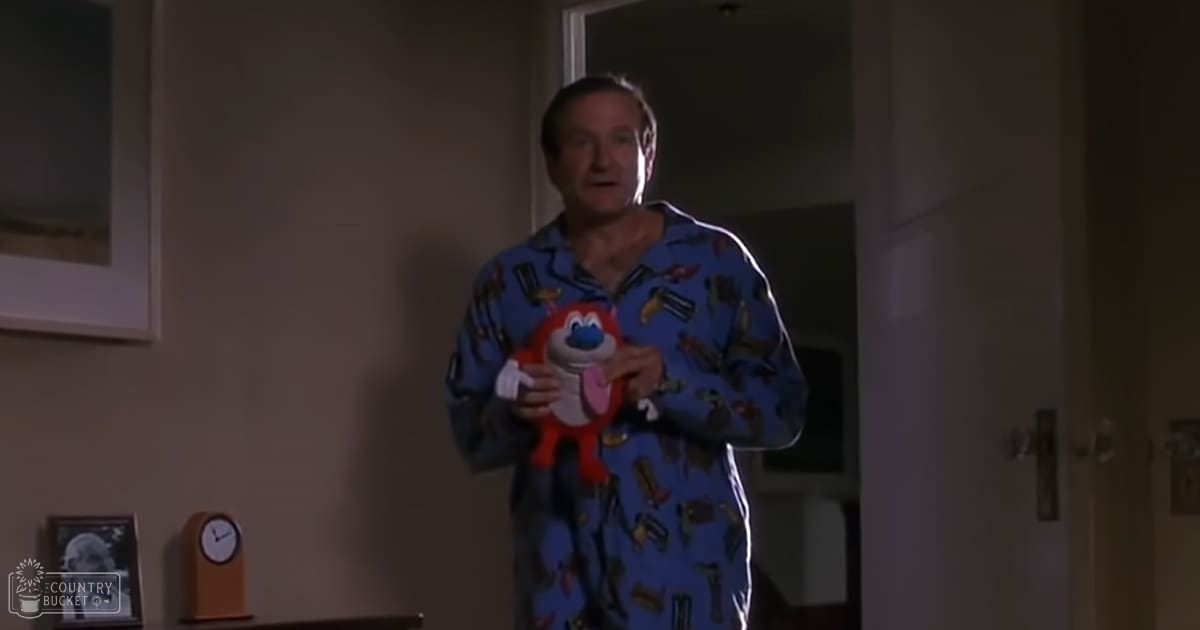 A middle-aged adult male in relaxed, loose-fitting blue pajama top with a pattern of various items, standing indoors near wall clock and framed picture.