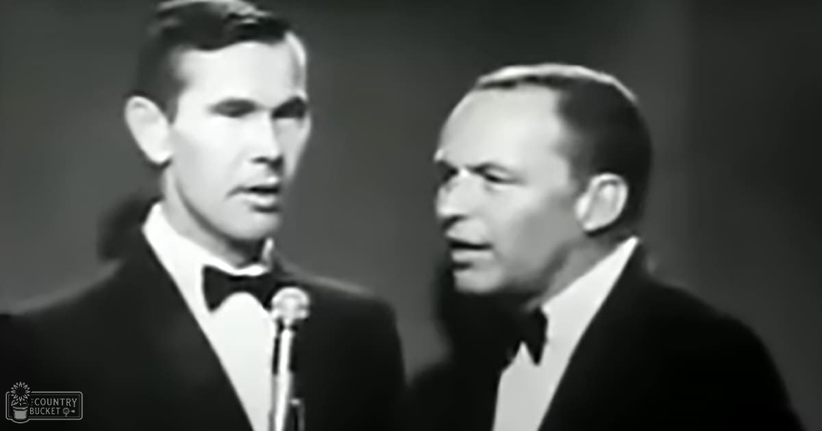 Two adult male performers in formal dark suits with white dress shirts and black bow ties on a stage setup under indoor lighting typical of mid-20th century performances.