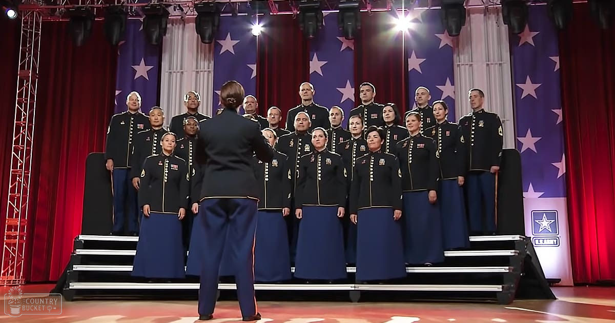 A choir performing in a theater or auditorium, wearing dark blue military-style uniforms with gold trim, during an indoor evening event.