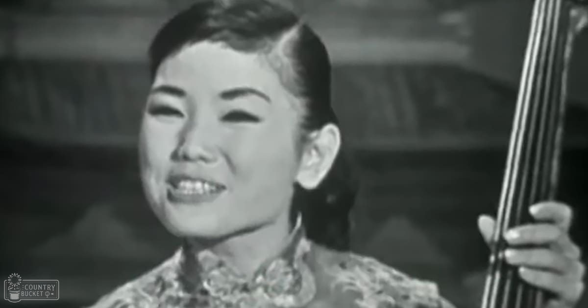 A young adult female in a traditional Chinese-style blouse with intricate floral embroidery and white fabric, set against an indoor background suggesting daytime lighting.