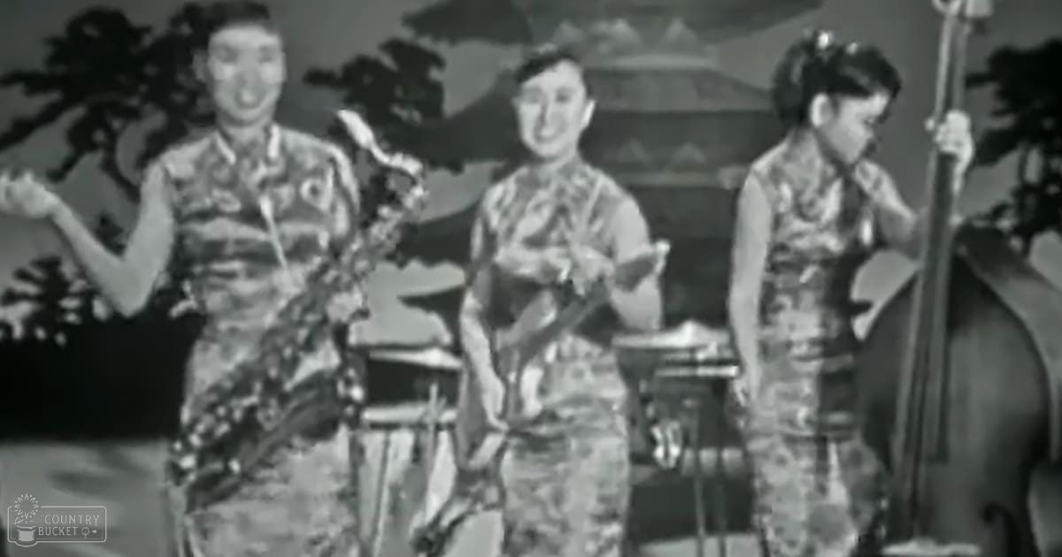 A musical performance scene with three adults playing instruments against a backdrop of trees and traditional structures, suggesting an indoor setting from the early-to-mid 20th century.