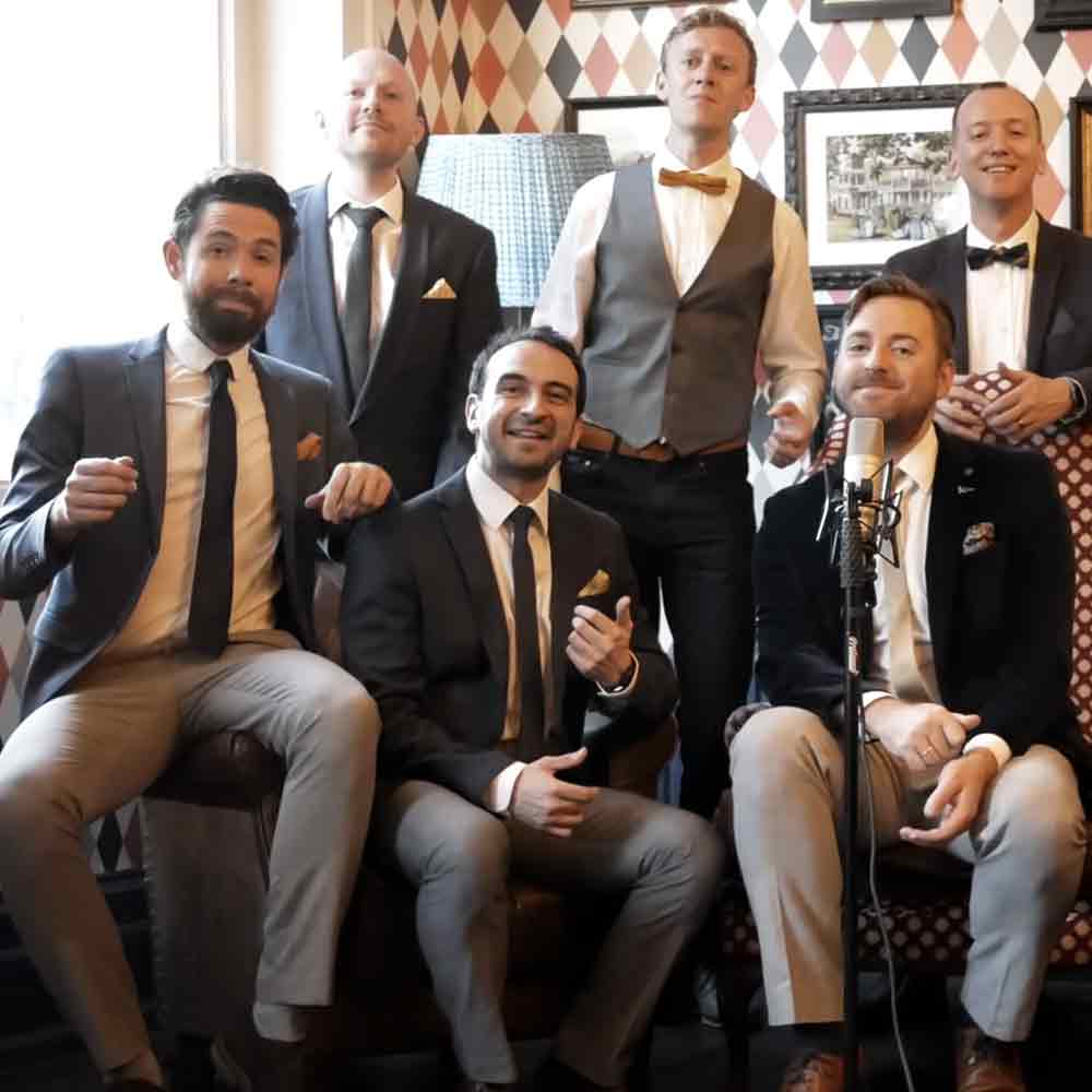 A group photo of a male musical ensemble in an indoor setting with natural light and geometric wall decor.
