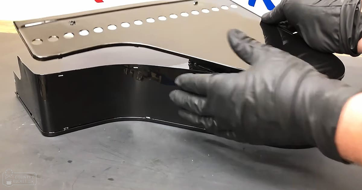 A person wearing black gloves works with a reflective, perforated metal piece on an industrial workbench.