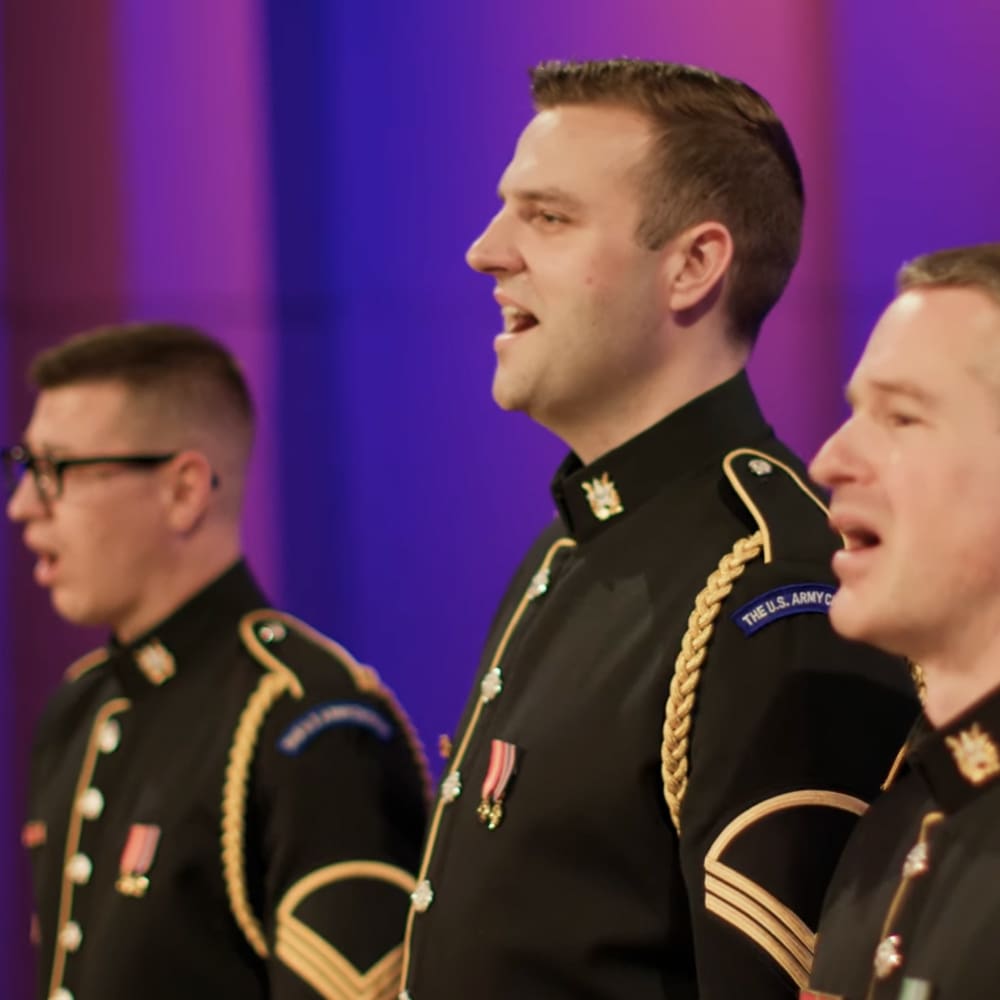 A group of uniformed individuals singing in an indoor setting, likely a concert hall or performance space.