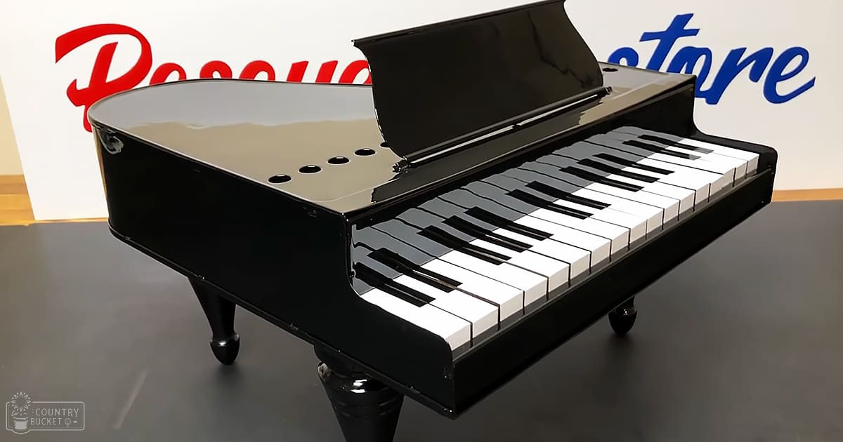 A black baby grand piano with white keys, glossy finish, and small wheels stands in a bright indoor store setting.