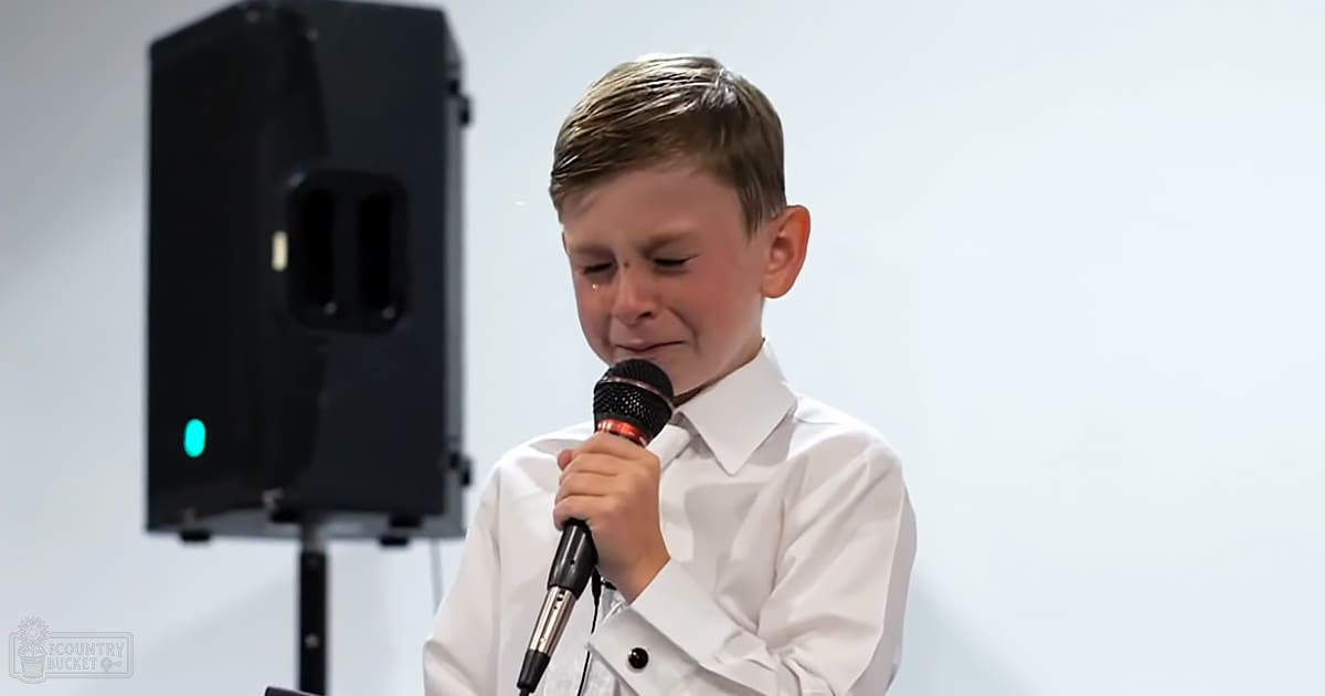 A young male child wearing a modern, white collared dress shirt indoors at an event.