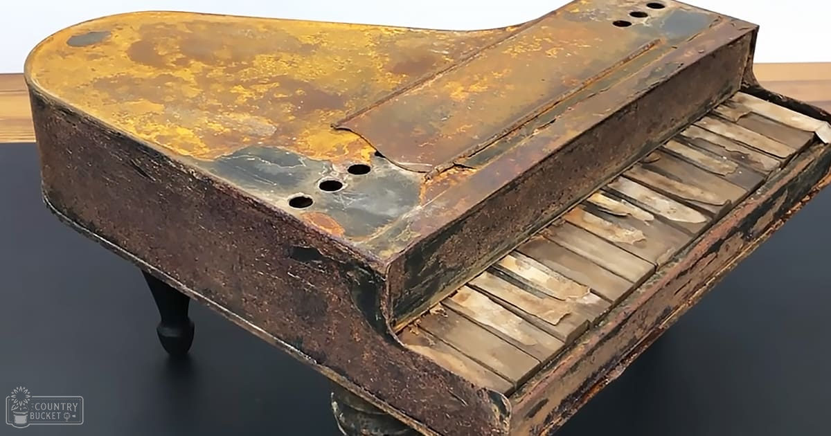 An old, heavily rusted piano with broken keys and peeling paint indoors on a dark-colored floor or table.