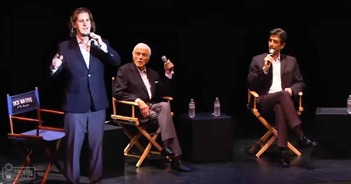 Panel discussion at an indoor event with microphones and director's chairs in a spotlighted setting.