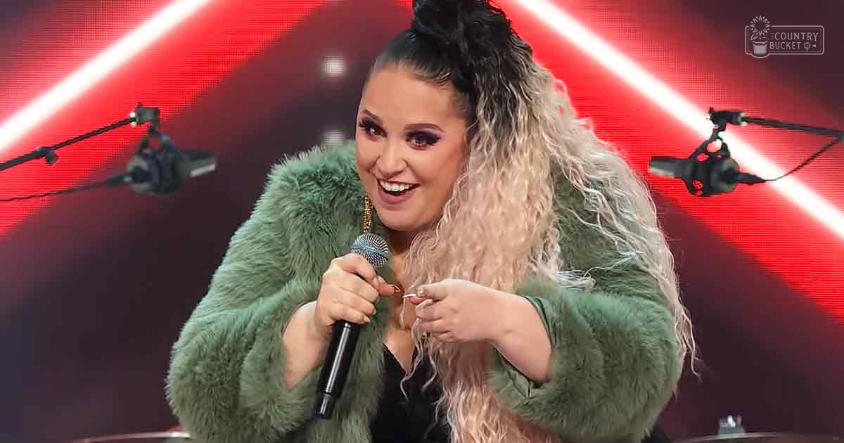 Young adult female performer in a studio setting, wearing a green faux fur coat with large hoop earrings.