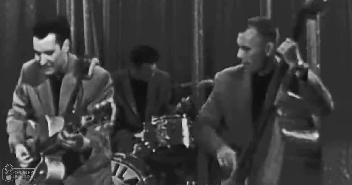 Musical performance with adult males in formal attire on an indoor stage with a guitar player and drum set.