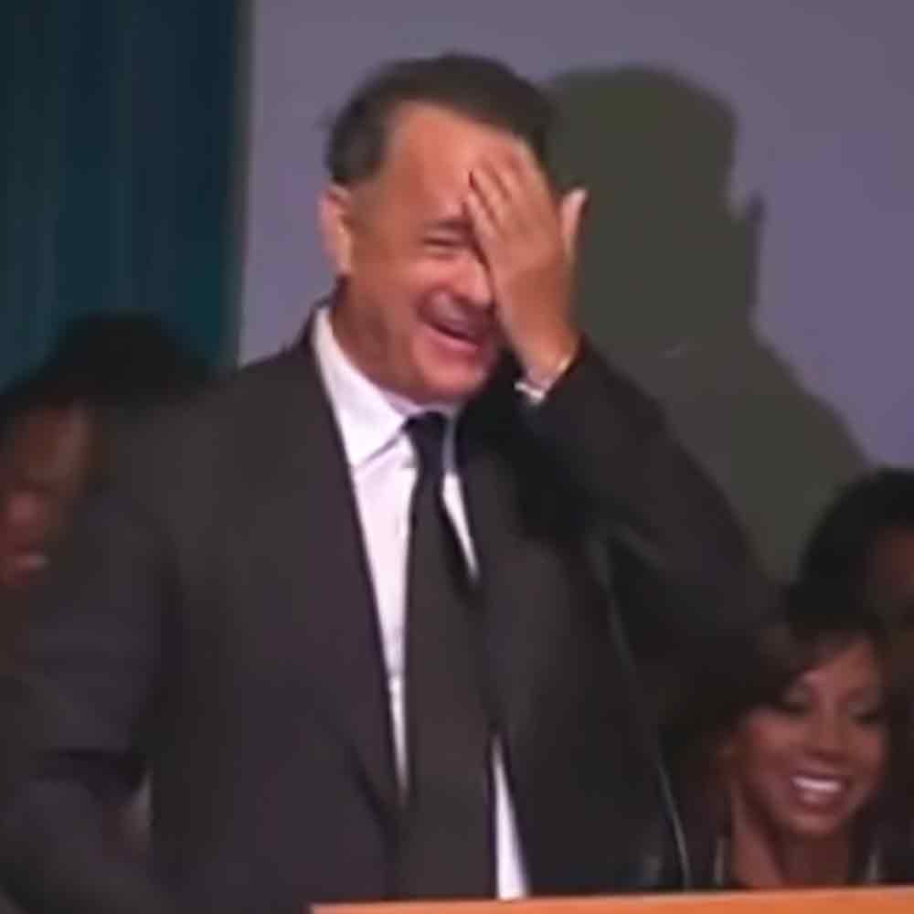 A middle-aged man in a black suit jacket stands indoors at what appears to be an awards ceremony.