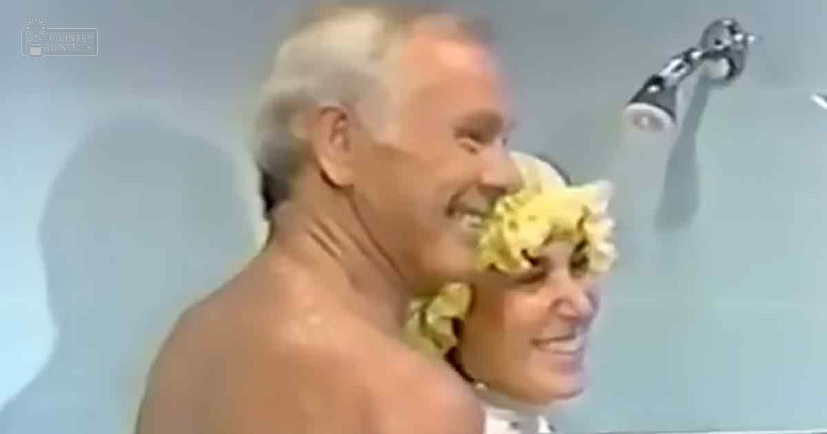 A middle-aged man stands in a shower with no visible garments, while a middle-aged woman wearing a white garment adorned with yellow flowers is present nearby.
