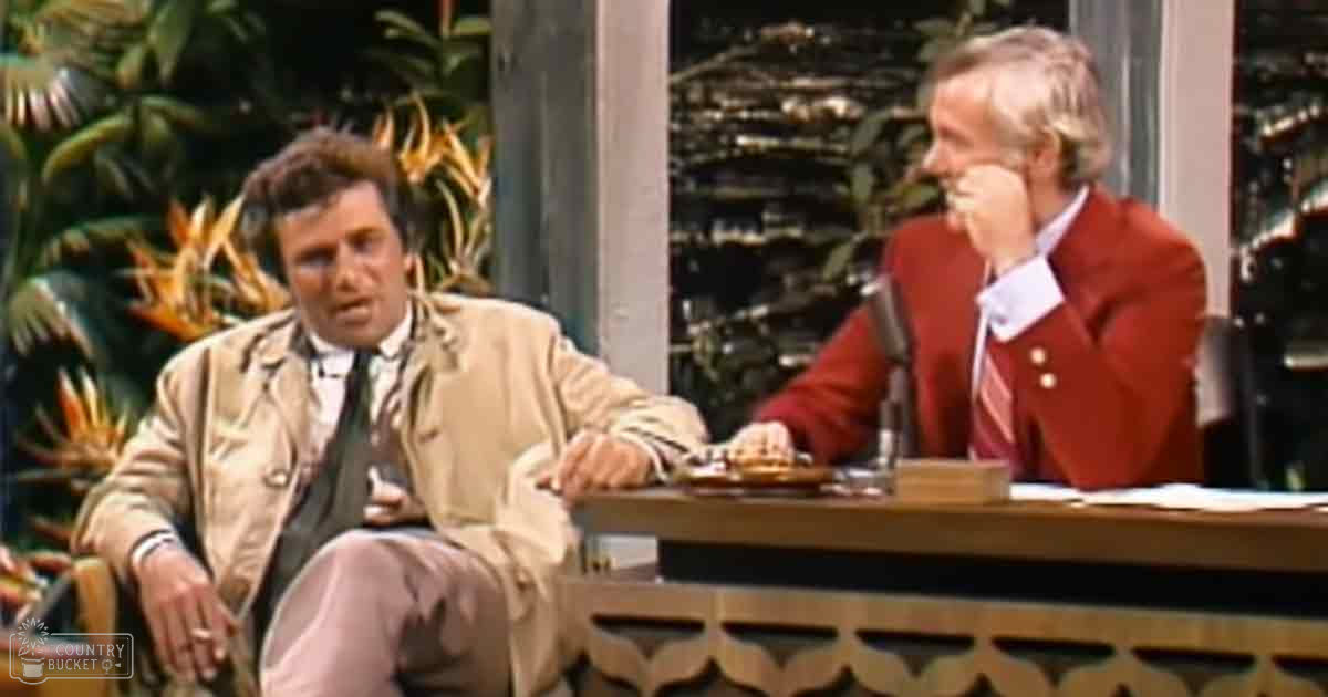 Two adults in a studio setting with wooden furniture and indoor plants; daytime lighting highlights their attire.