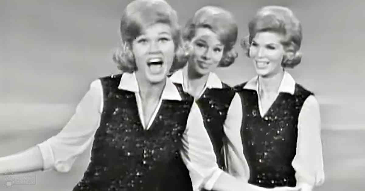 Three adult females in a studio setting, each wearing a white shirt under a black sequined vest with high collars and long sleeves, against a plain light-colored backdrop.