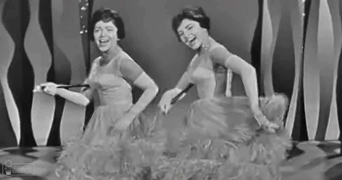 Two women in a studio setting, dressed in short-sleeved dresses with fitted bodices and flared skirts, possibly made of tulle or chiffon.