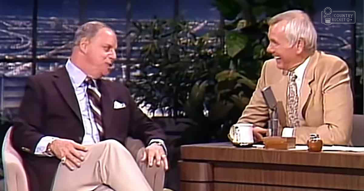 A late 20th-century talk show set with two older adult male speakers seated at a wooden desk, surrounded by artificial stage lighting and indoor studio decor.