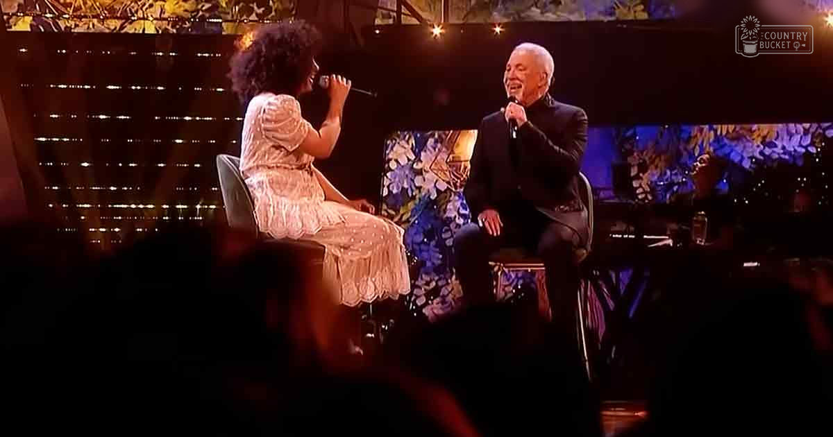 A performance scene at an indoor event with two adults, one in a light-colored dress and another in a dark suit, with decorative chairs and abstract stage designs in warm tones.