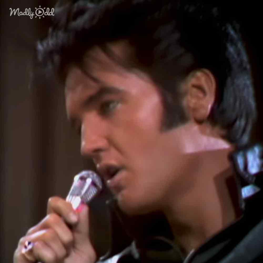 A young adult male singing into a dark microphone in an indoor setting with dim lighting.