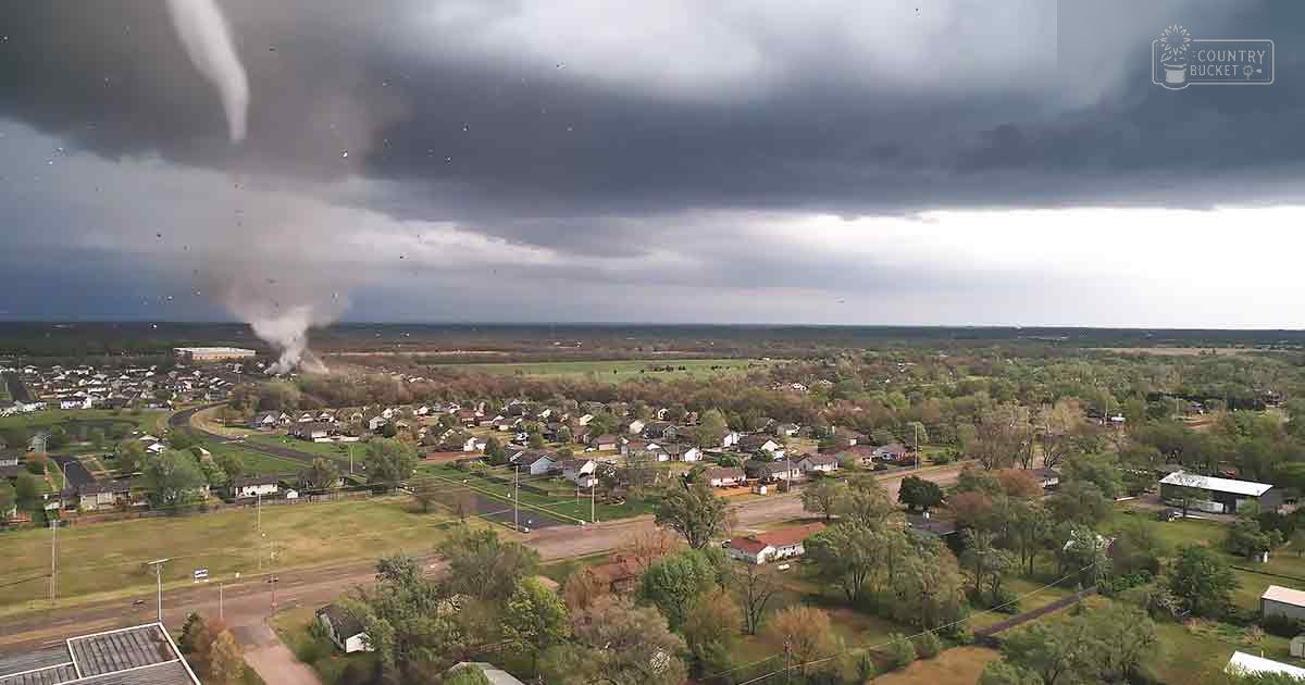 A tornado dominates a suburban landscape with residential houses and overcast skies.