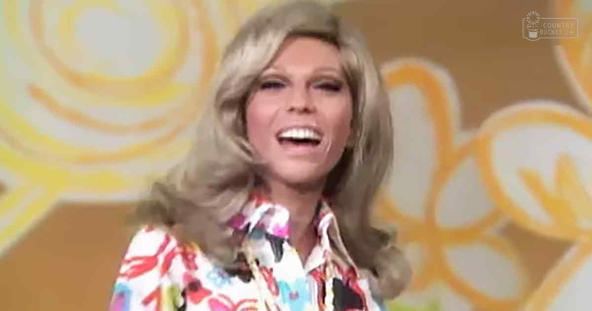 Middle-aged adult female wearing a floral blouse with relaxed fit and long sleeves, set against an indoor backdrop with abstract patterns.