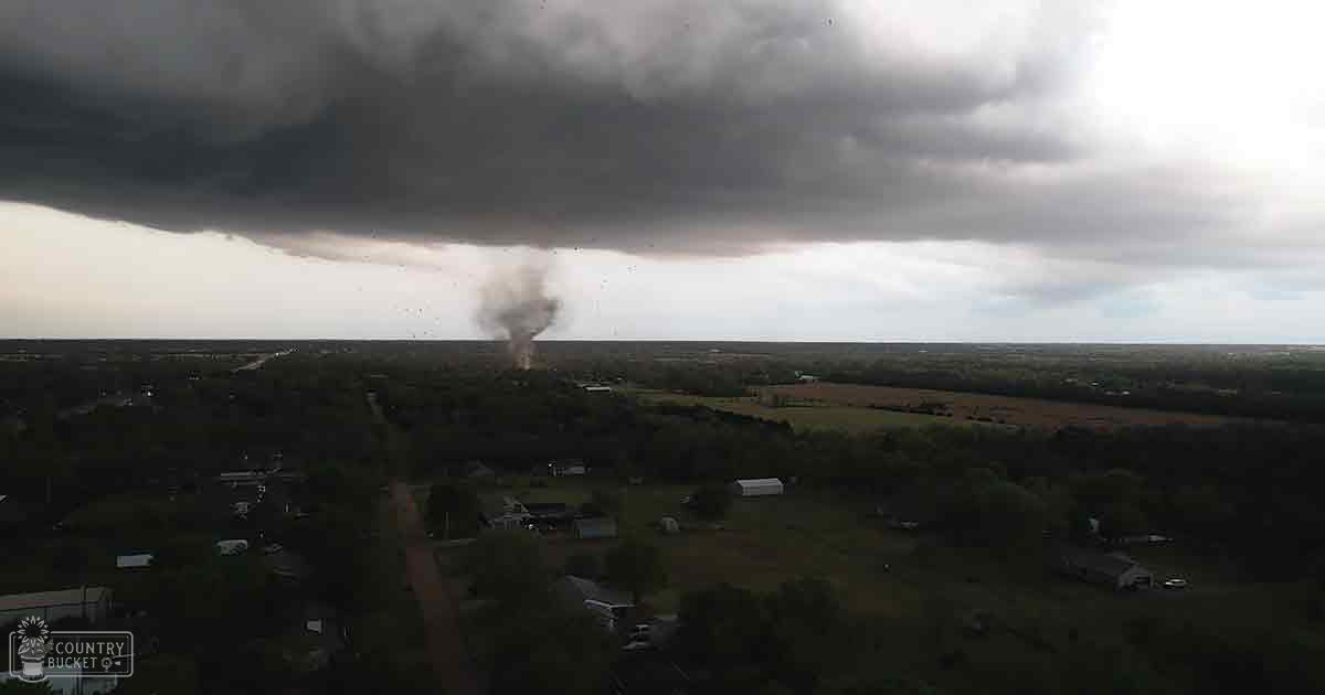 Tornado forming in a rural landscape with scattered houses under an overcast sky during spring or summer.