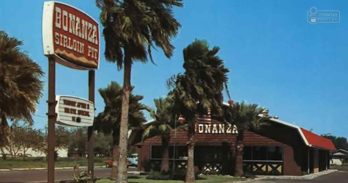 Palm trees, clear blue sky, Bonanza Sirloin Pit sign on sunny day with red-roofed building in background.