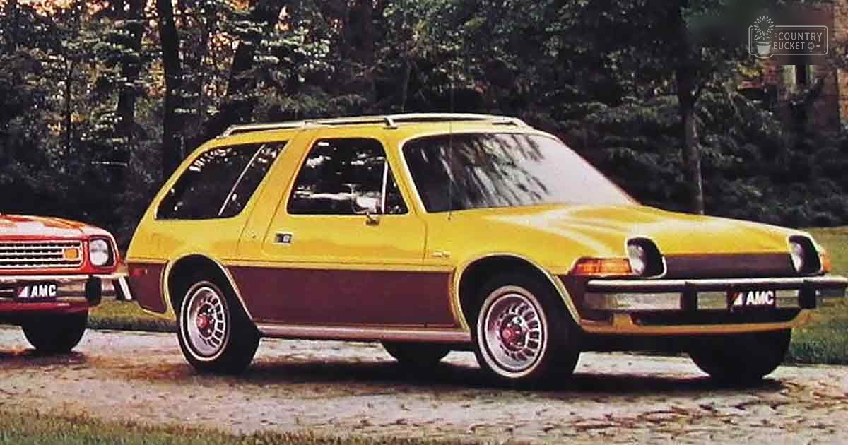 Two vintage AMC cars, one yellow with burgundy accents, parked outdoors in a wooded area during autumn.