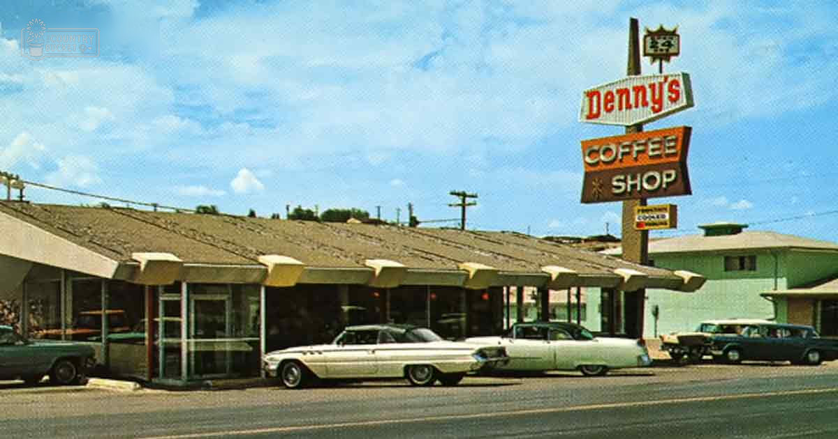 A sunny day scene with vintage 1950s-era cars parked outside Denny's Coffee Shop in a suburban area.