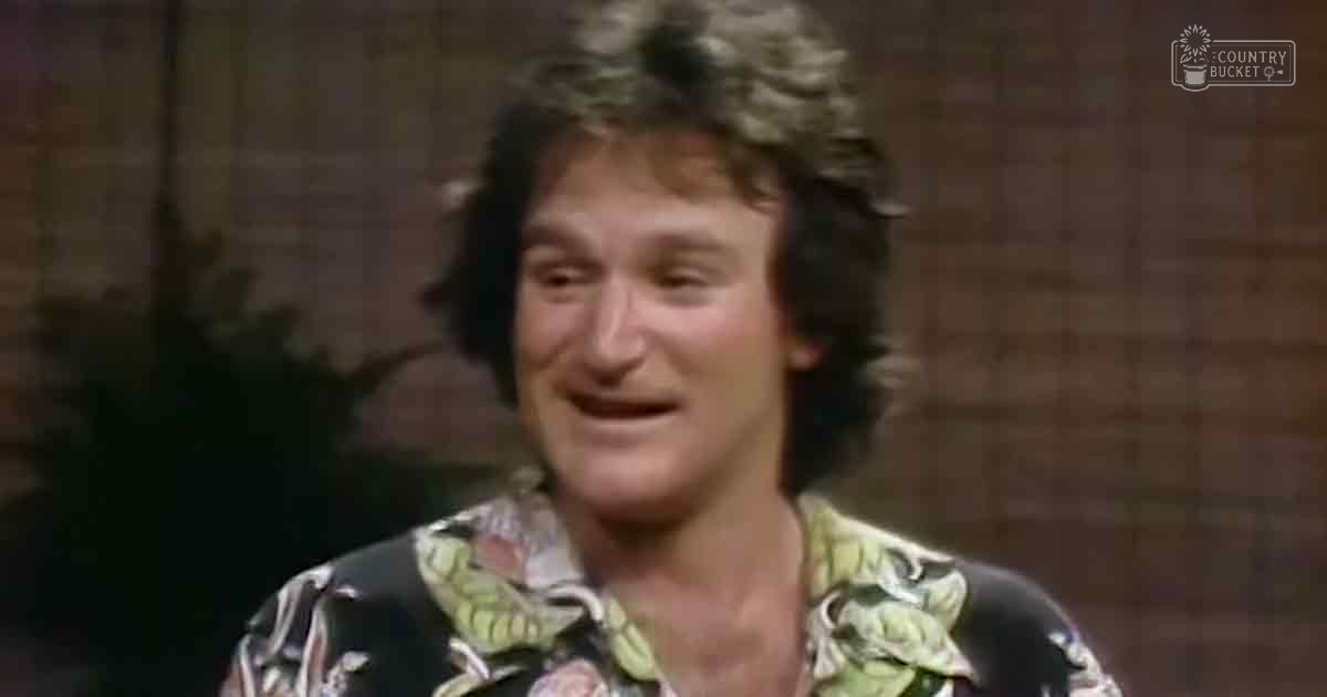 A middle-aged man wearing a patterned floral shirt indoors, surrounded by out-of-focus greenery.