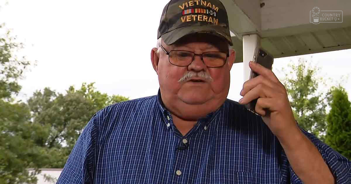 An older adult male wearing a blue striped button-up shirt with a collar and long sleeves, holding a smartphone in an outdoor residential area with trees and a porch-like structure; 'Madly Odd' text is visible.
