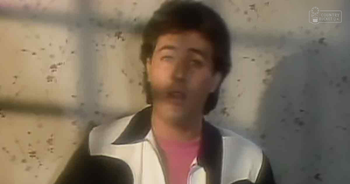 A young adult male wearing a white jacket with black lapels over a pink shirt, possibly from the late 1970s or early 1980s, indoors against a wall showing signs of wear.