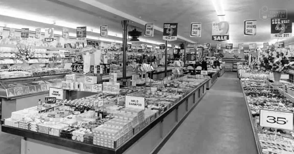 Vintage grocery store interior with mid-20th-century style shelving, promotional signs, and decorative flowers in vases.