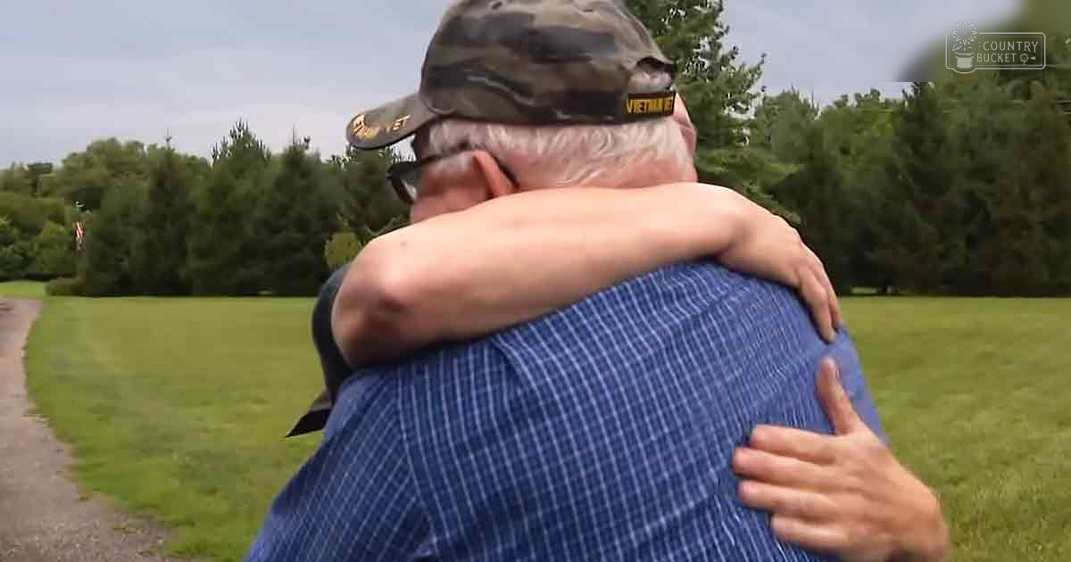 Older adult male in a park-like setting with green grass and trees, wearing a camouflage baseball cap and blue plaid shirt, late afternoon light suggesting spring or summer season.