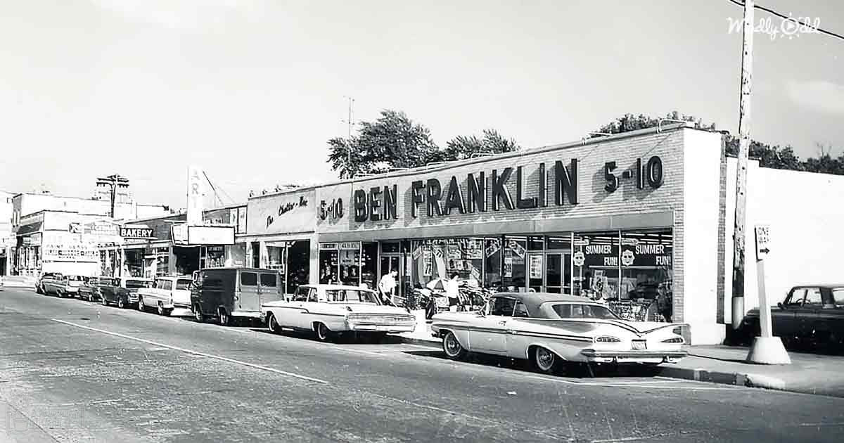 Adult male entering a Ben Franklin 5-10 store in an urban area with vintage cars parked outside during daytime.