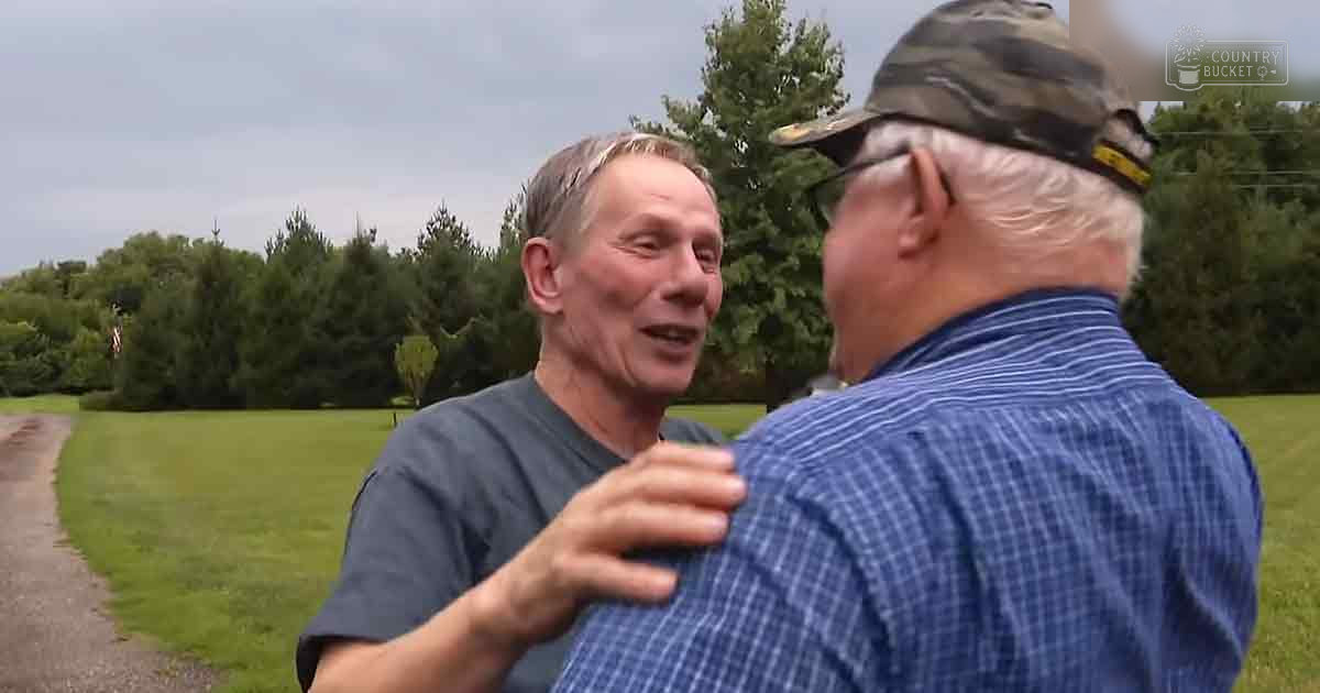 Two older adults in a rural outdoor setting with greenery, trees, and an overcast sky.
