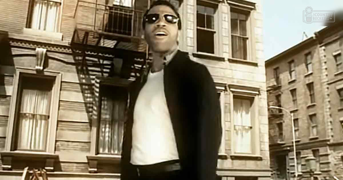 Young adult male wearing a white t-shirt and black jacket, sunglasses on, urban residential neighborhood with brick buildings and fire escapes. Sepia tone overall, late afternoon light.