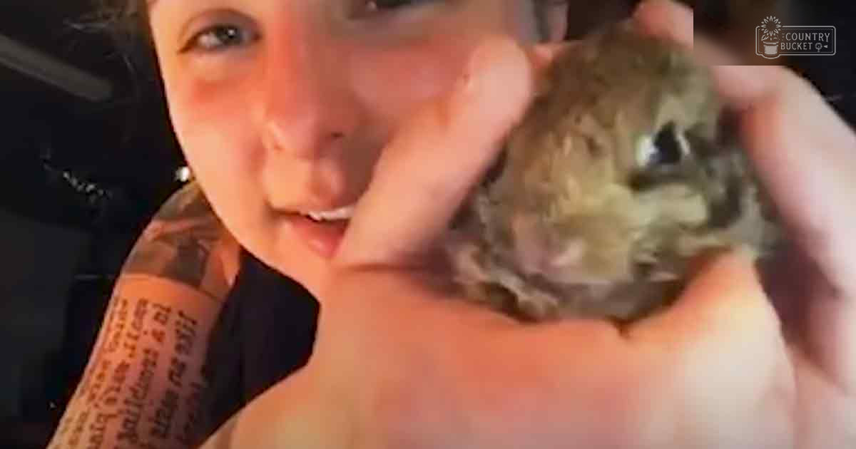 A young adult female holds a juvenile rodent in an indoor setting with dim lighting, suggesting evening or night time.