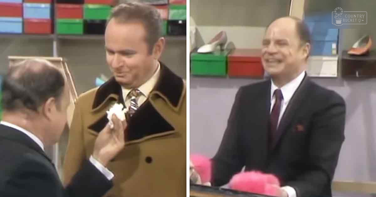 Talk show set with two adults in dark suits; shelves of colorful boxes, shoe displays, pink fluffy object near older male