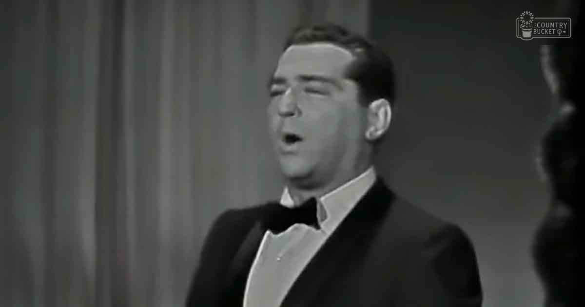 Adult male in a formal black tuxedo indoors with plain curtain backdrop