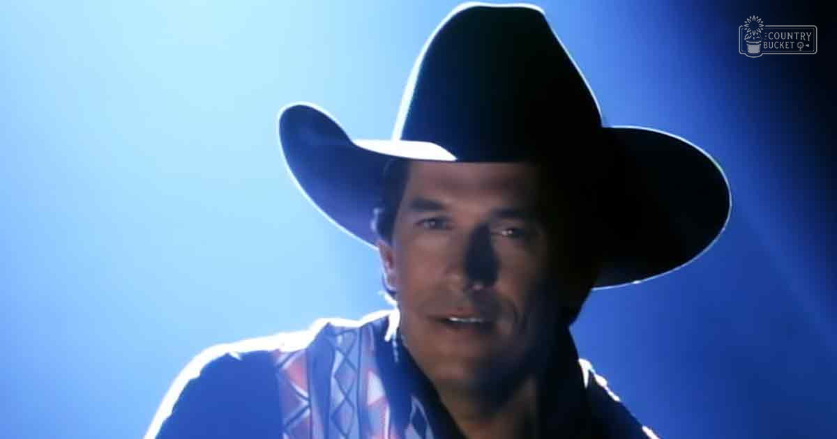 A middle-aged adult male wearing a fitted cowboy shirt with intricate geometric patterns inspired by Native American motifs stands indoors under dramatic blue lighting.
