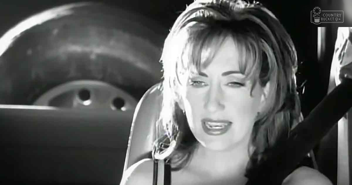 A young adult female singing on stage with a microphone in front, wearing a sleeveless black dress under focused lighting.