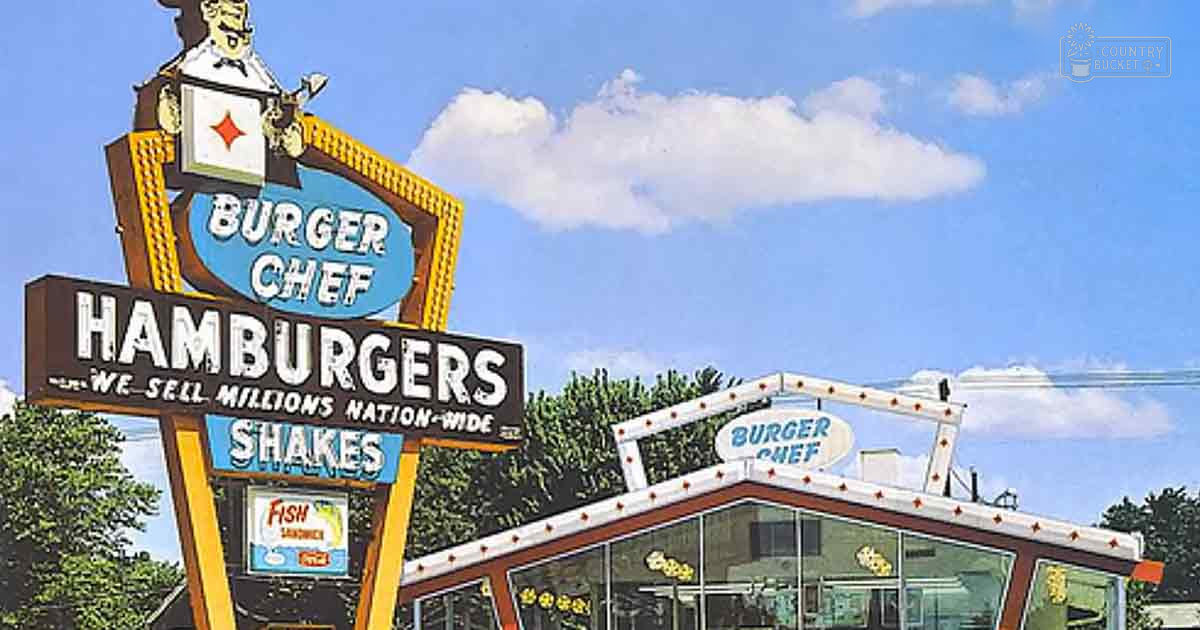 Burger Chef restaurant sign with text indicating 'Hamburgers,' 'We Sell Millions Nation-Wide,' and 'Shakes,' set against a backdrop of blue sky, scattered clouds, and trees in an outdoor area.