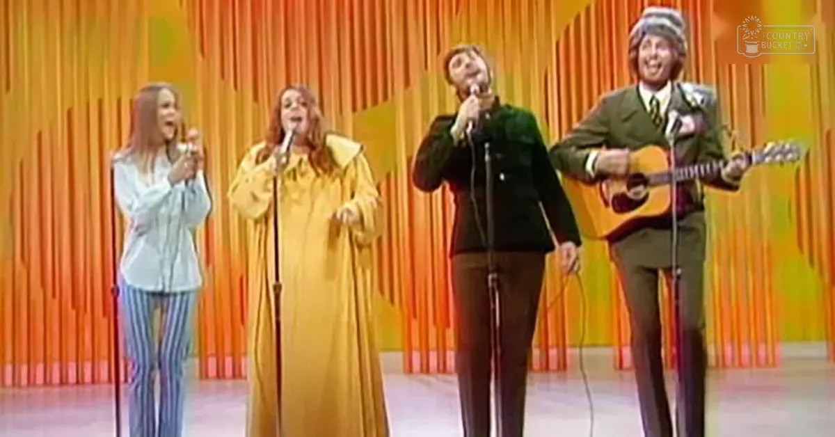 Musical performance group from the 1970s in an indoor studio with bright orange curtains and even lighting.