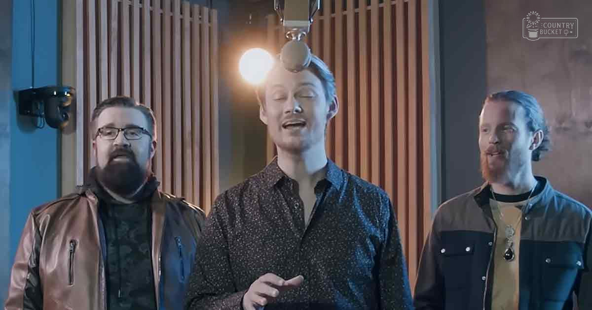 Adult males wearing casual attire with brown leather jackets, patterned shirts, and mustard yellow shirts in a recording studio setting with wooden acoustic panels and studio equipment.