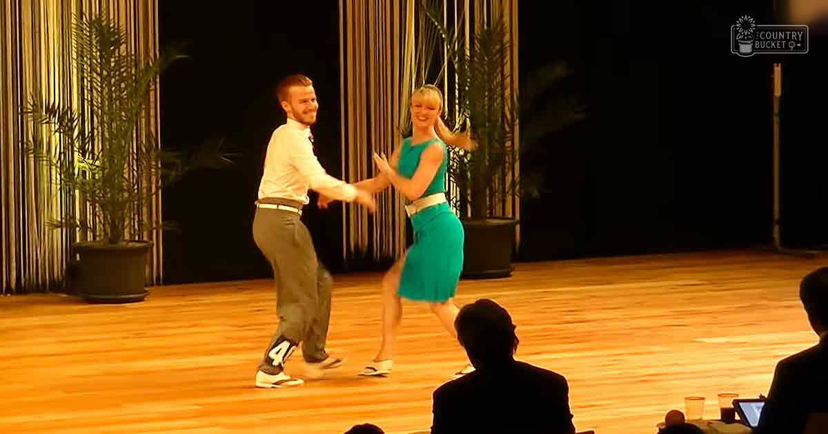 A dance performance with male and female dancers in an indoor auditorium setting under stage lighting.