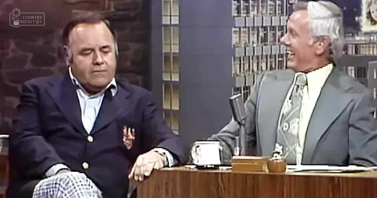 Talk show set with two individuals seated at a desk in an indoor studio environment, with mid-20th century style furniture and decor.