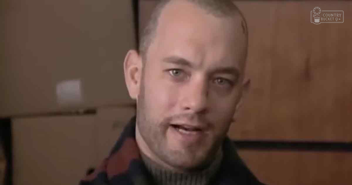 A middle-aged adult male wearing a dark-colored, ribbed turtleneck sweater indoors with wooden cabinetry and light switch plate in the background.