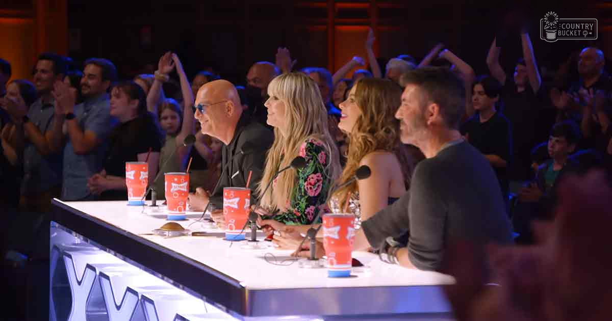 A panel discussion at an indoor event, likely a talent show or competition, with audience clapping and panelists seated around a long white table with microphones and refreshments.