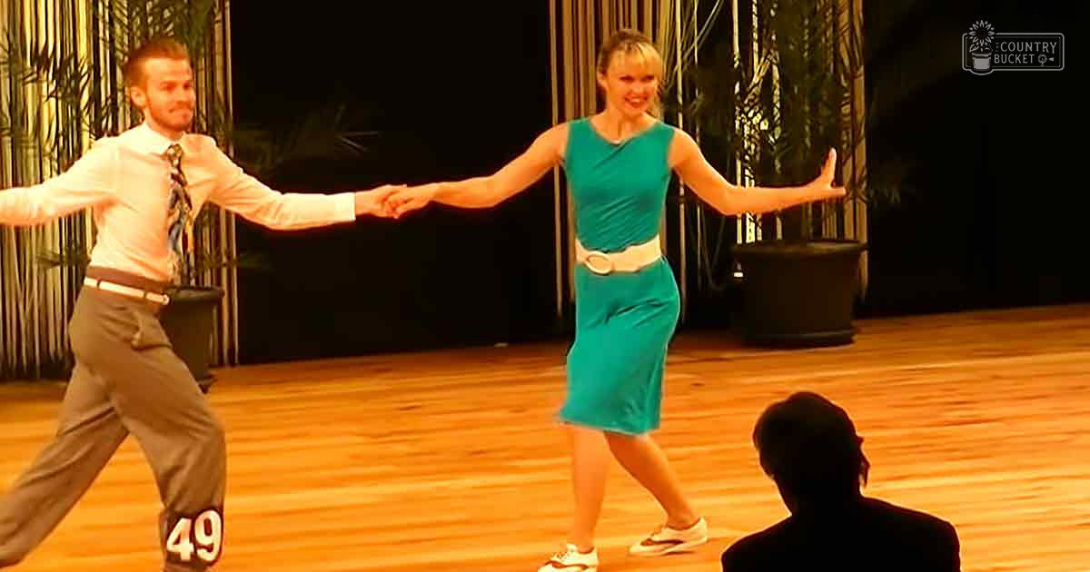 Adult male dancers in a dance studio, teal dress with white belt, wooden floor, indoor setting at night.